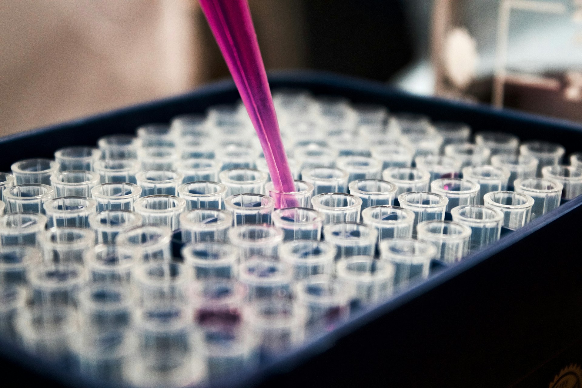 Biotech researcher in a lab coat handling sample vials at a well-lit bench with equipment in the background